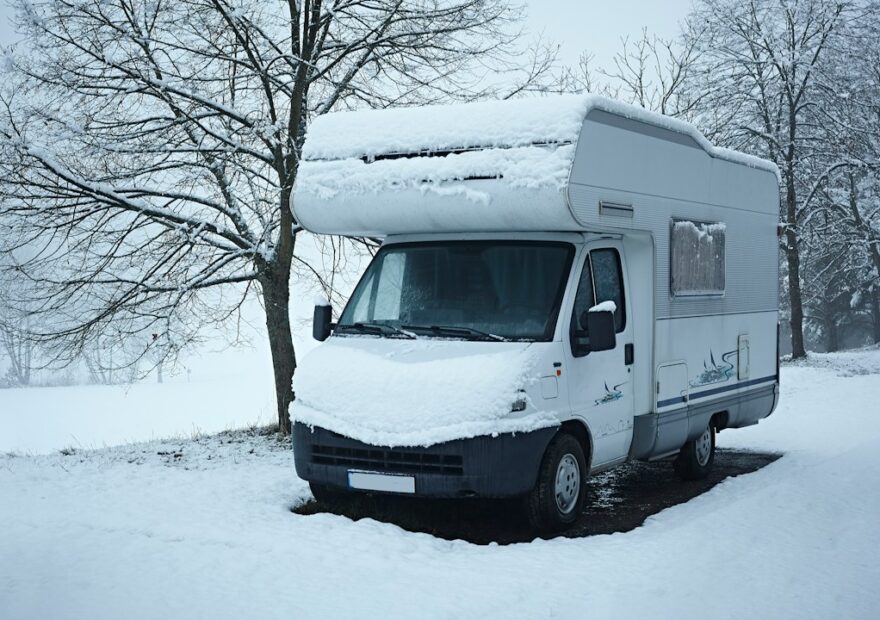 Vit husbil täckt av snö uppställd vid ett träd på vintern